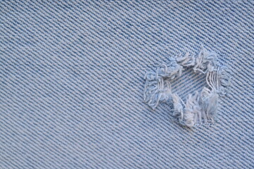 torn light grey denim surface, denim fringe , hole macro texture of blue denim, torn blue denim texture as background photo close up from above	
