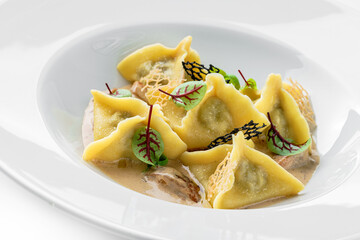 Ravioli with sauce decorated with greens in plate isolated on white background. Italian dishes, top view, close up