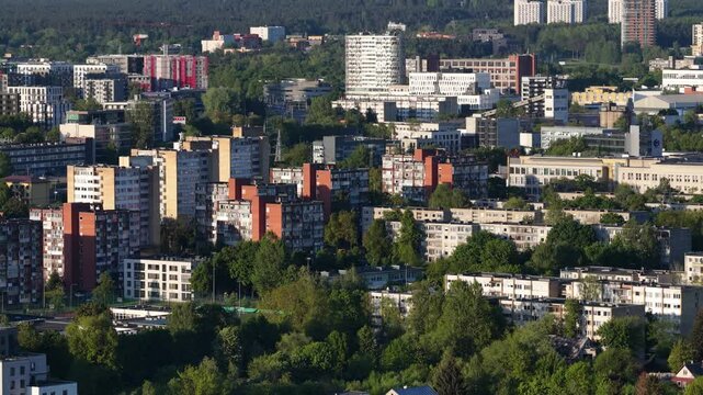 Aerial view of Vilnius showcasing a mix of Soviet-style residential buildings and newer urban developments, surrounded by greenery and forested hills.