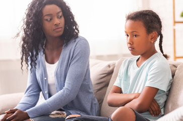 Disobedient child. Disappointed black mother looking at her little daughter with reproach, sitting...
