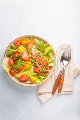 Grilled salmon fillet lies on a fresh salad of lettuce, cherry tomatoes, and arugula, served on a plate, light grey background, a healthy and delicious meal