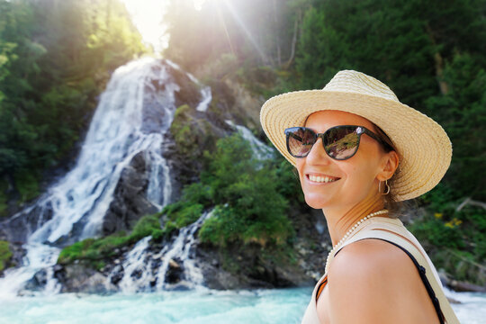 Portrait young adult happy smile woman wear hat sunglasses enjoy hiking Haslach village Staniskabach Schleierfall waterfall Tyrol Austria Austrian Alps. Female person joyful journey. Summer vacation