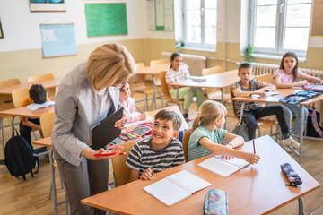 mature woman teacher checking school kids homework in the classroom