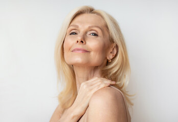 Portrait of attractive senior woman with bare shoulders and perfect skin posing over white wall...
