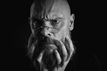 Black and white portrait, serious bald man with beard and glasses looking intently at the camera,...