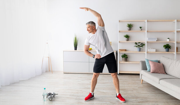 Sport on retirement. Active mature man doing flexibility exercises for healthier living during home workout. Man leading sporty lifestyle, training in living room interior, copy space, panorama - Powered by Adobe