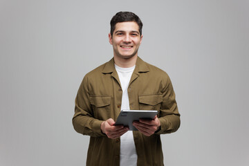 Smiling man engaged in a digital moment while holding a tablet in a neutral backdrop at home