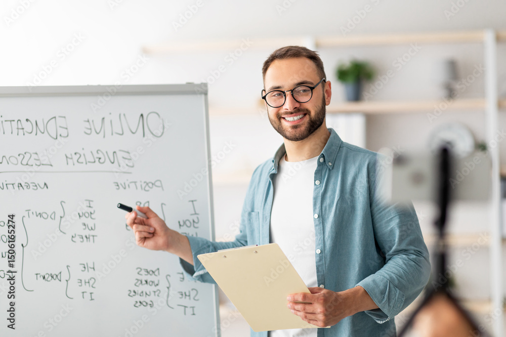 Poster portrait of happy young male teacher standing near blackboard with english grammar rules, conducting