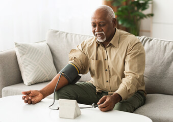 Mature African American Man Measuring Arterial Blood Pressure With Sphygmomanometer Medical Device...