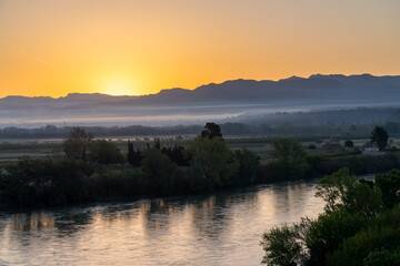 Sunrise over a river valley with mountains in the background.