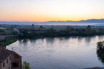 Obraz premium Sunrise over a river valley with mountains in the distance.