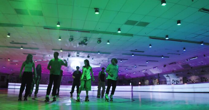 Colorful disco lights with roller skaters dancing together in unison - wide, steady cam shot