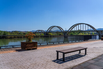 Scenic view of a bridge over a river with a bench and planter in the foreground.