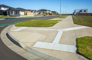 A newly constructed suburban sidewalk featuring tactile ground surface indicators (TGSIs) for...