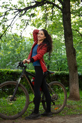 Fototapeta premium Beauty smiling woman long brown hair biking on bicycle on spring trees background and looking. Enjoying fun happy girl outdoors. Female cyclist riding in green park. Full lenght portrait