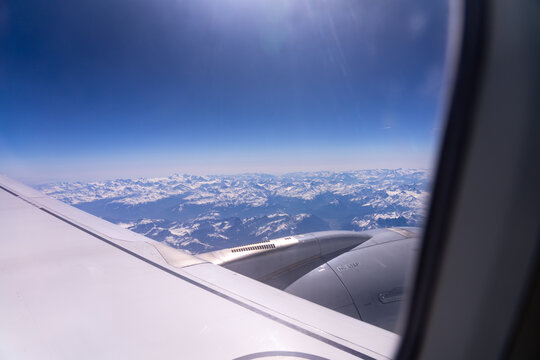 Aerial view of snow-capped mountains from an airplane window on a sunny day.
