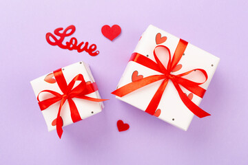 Festive gift boxes with red hearts on color background, top view