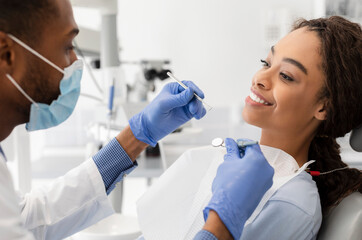 African young woman attending dentist, doctor in mask and gloves making check up, side view, close...