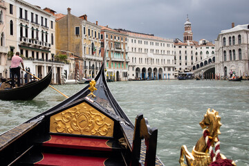 Decorative front of a gondola with golden emblem and view of Venetian architecture along the Grand Canal © Vlad Yakubovskiy