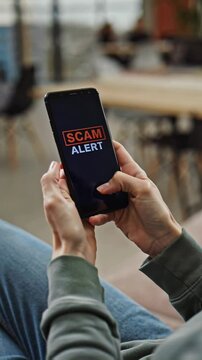 Close-up of hands holding a smartphone displaying a scam alert notification. Digital security awareness and caution, fraud alert