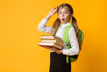 Back To School. Surprised Primary School Girl Carrying Stack Of Heavy Books Over Yellow Background....