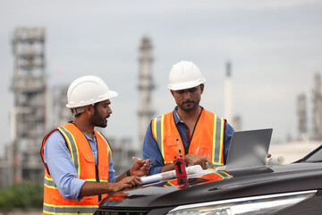 Industrial engineer with orange safety vest and white hardhat work on front hood of car at Refinery and gas petrochemical plant