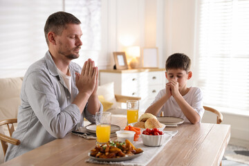 Father and son praying before dinner at table indoors