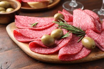 Slices of delicious sausage with olives and rosemary served on wooden table, closeup