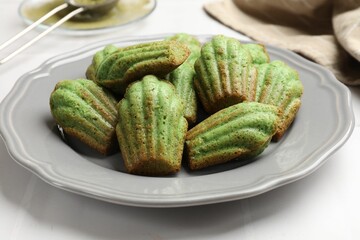 Tasty matcha madeleine cakes on white tiled table, closeup
