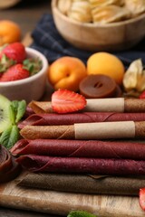 Tasty candied leather rolls, fruits and berries on wooden table, closeup