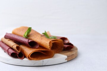 Delicious fruit leather rolls and mint on light table, closeup. Space for text
