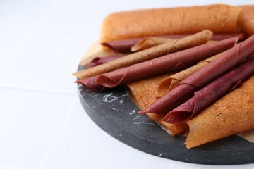 Delicious fruit leather rolls on white table, closeup. Space for text