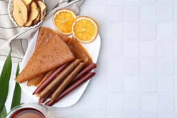 Tasty fruit leather rolls and orange slices on white table, flat lay. Space for text