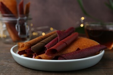 Tasty fruit leather rolls on wooden table, closeup