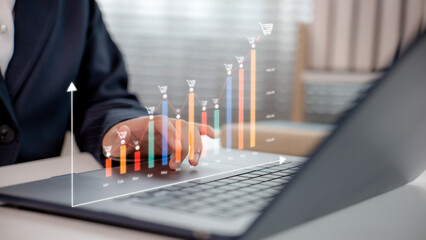 Businessman using laptop with rising monthly ecommerce sales chart and shopping cart icons,...