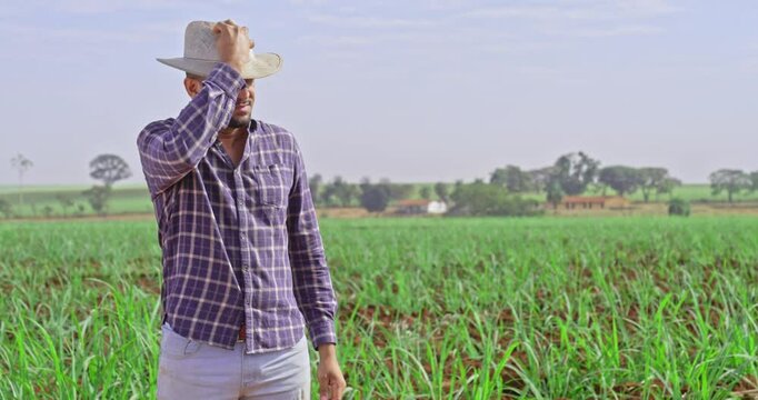 Young latin farmer wearing hat standing in field smiling with arms crossed.