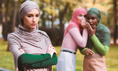 Bullying. Fake Friends Talking About Unhappy Muslim Woman Standing Alone In Park Outdoor. Female...