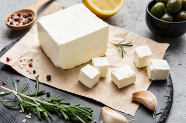 Block of feta cheese, olives, herbs and spicies on board over concrete background. Traditional greek food concept