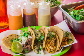 A colorful presentation of tacos filled with various meats and garnished with fresh vegetables, accompanied by sauces and lime for a delightful culinary experience.