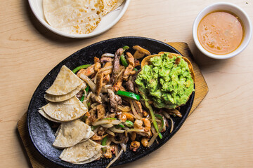 This enticing dish displays authentic fajitas, garnished with fresh avocado, vibrant peppers, and served with tortillas, reflecting a joyful culinary and dining experience.
