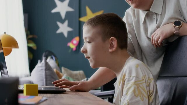 Slow motion of mother assisting teenage son with disability studying on wireless laptop at home table