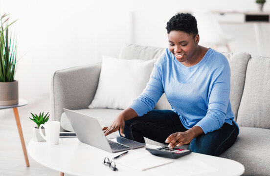 Business Concept. Smiling African American female accounting analyst calculating income and expenses for financial report and banking investment. Black woman using laptop computer at home office