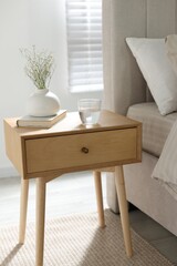 Bedside table with flowers in vase, glass of water and book near bed indoors