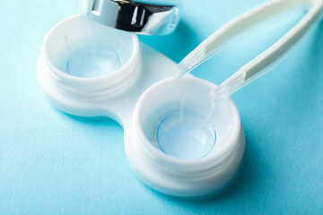 Contact lenses in case and tweezers on light blue background, closeup