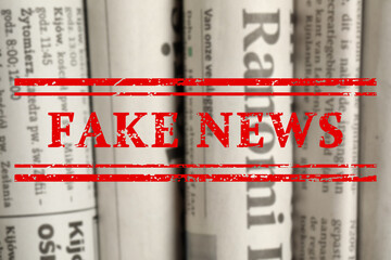Red Fake News stamp and newspapers in different languages as background, closeup