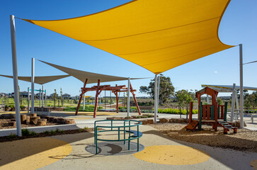 A colorful suburban playground featuring fabric shade sails, and soft fall surfacing, designed to provide sun protection and safe outdoor recreation in a newly developed neighborhood in Australia.