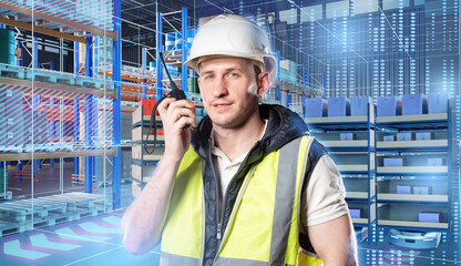 Warehouse worker in a safety vest and helmet uses a walkie-talkie in a high-tech automated storage...