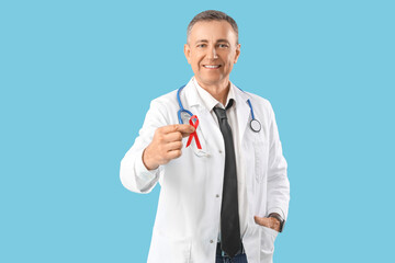 Mature male doctor with red ribbon on blue background. World AIDS Day concept