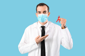 Young male doctor with face mask and red ribbon on blue background. World AIDS Day concept