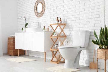 White toilet bowl, shelving unit and chest of drawers with sink near white wall in restroom